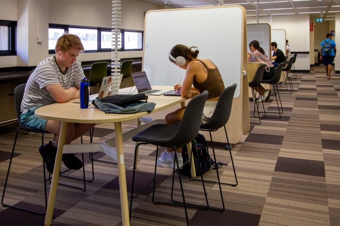  Students studying on high chairs and long table near a tepee presentation board.