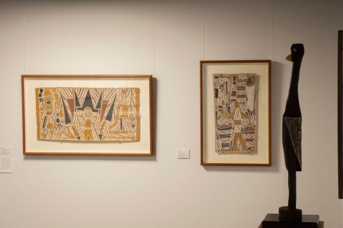 A photo of a gallery space with two framed artworks to the left and centre, and a wooden sculpture on the far right. 