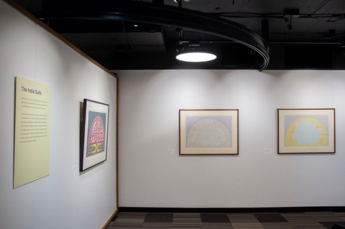 A gallery space with a view of two adjascent walls. Both walls display framed paintings with muted colours and soft shapes. 