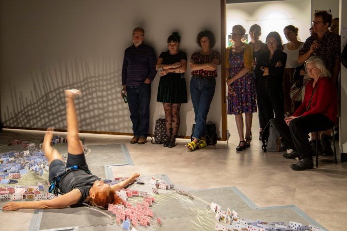 Crowd watching Vicki Van Hout peformace as she is lying on floor surrounded by playing cards