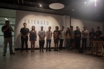 A dozen university student stand in a row in front of a gallery wall that reads "Extended Reality"