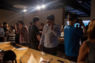 Photo of an exhibition opening event. A crowd of people gather in a gallery space, some of the are wearing VR headsets, others are socialising.