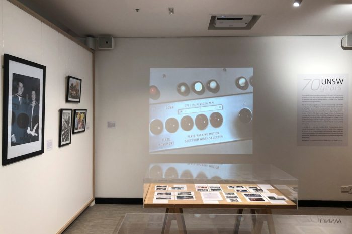 Framed photographs hanging on a white wall with a glass display cabinet to the right .