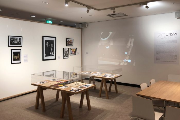 Framed photographs on the back wall with two display cases and a wooden table to the right.