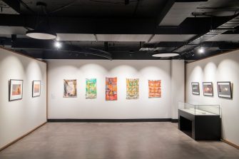 A wide-angle photograph of a gallery space with several colourful rectangular artworks mounted on the wall.