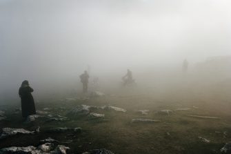 Several people in dark clothing stand on a rolling hill covered in a thick mist