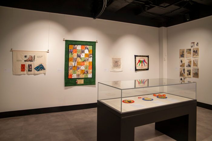 A room with two walls lined with stitched artworks and banners. A display case contains small, colourful round rosettes.