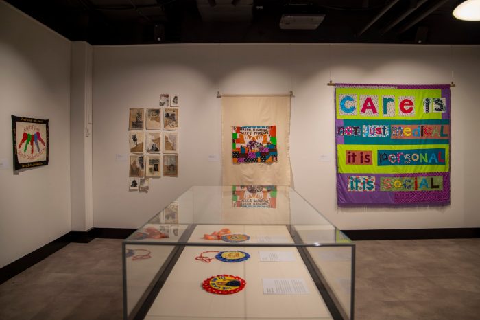 A room with two walls lined with stitched artworks and banners. A display case contains small, colourful round rosettes.