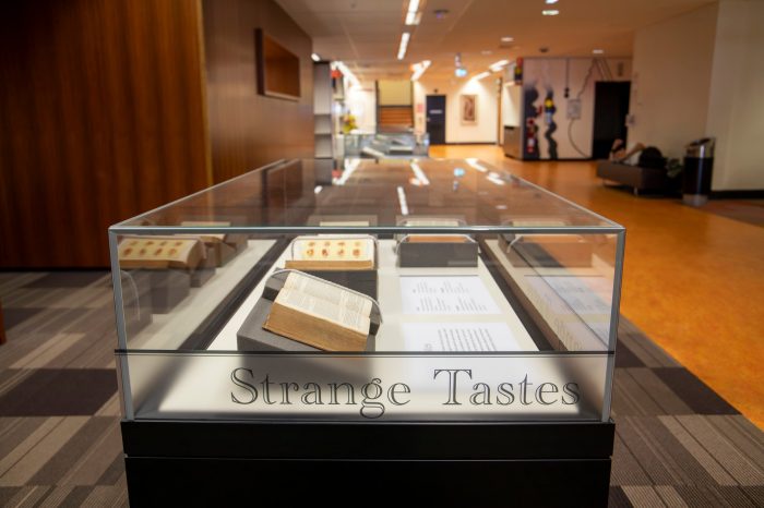 A photograph of a display case featuring four books propped open to display recipes and food illustrations