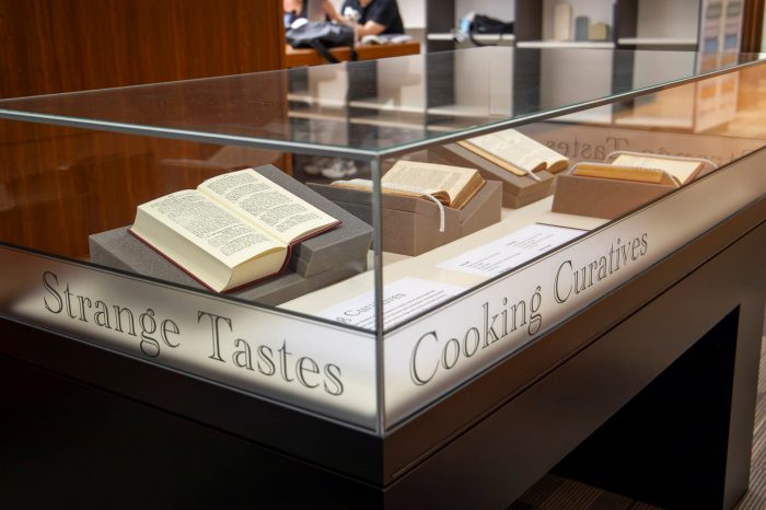 A photograph of a display case featuring four books propped open to display recipes and food illustrations