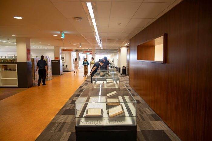 A photograph of students looking at display cases featuring books propped open to display recipes and food illustrations