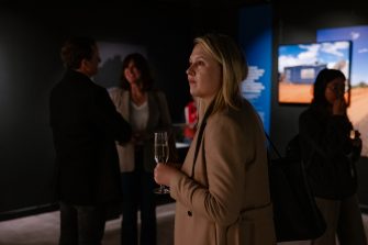 A woman holding a glass of champagne views artworks in a darkened gallery space