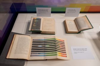 A display case with three valuable books. The books are opened, showing images of the colour spectrum.