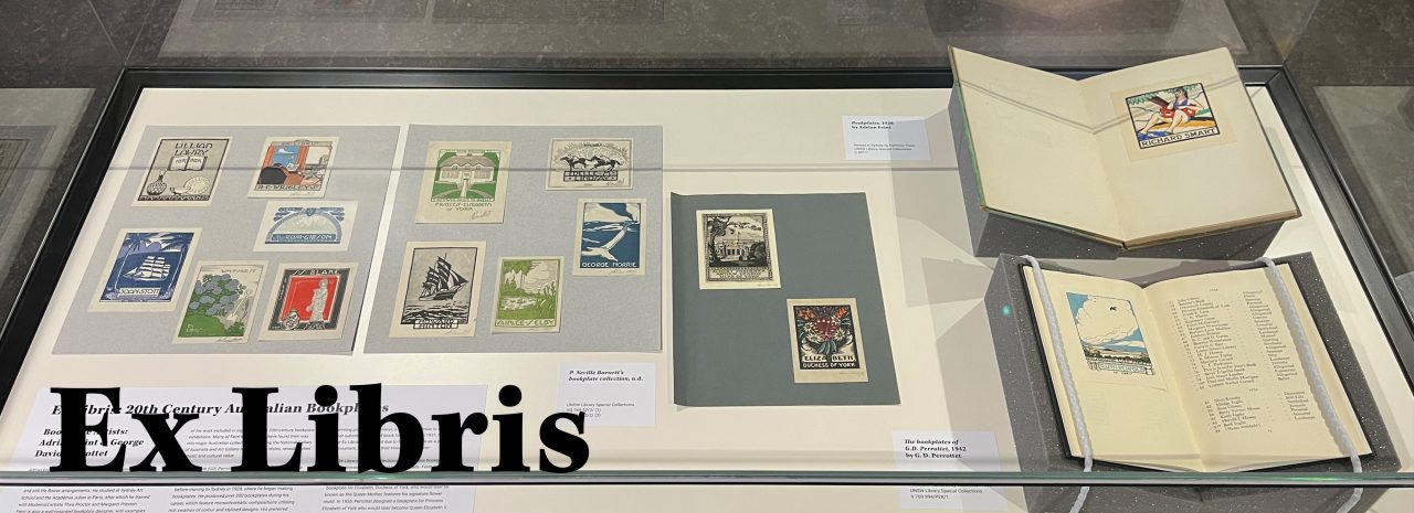A glass display case contains small multicoloured prints affixed to sheets of paper. Two books supported by grey foam wedges are propped open to pages featuring a colourful, floral bookplate and a series of two black and white bookplates of an urn.