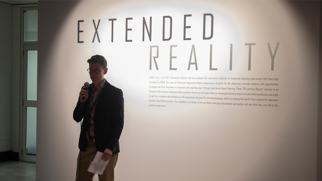 A person stands with a microphone in hand in front of a wall with the text “Extended Reality”